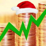 A stack of coins trending upward with an arrow and a Santa Claus hat sitting on the coins.