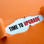 A tear through a piece of orange construction paper, revealing “time to upgrade” in black and red text.