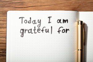 The words “Today I am grateful for” written inside of a journal next to a pen.