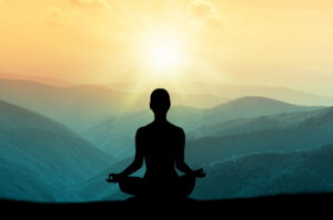 A person sitting in padmasana position while overlooking the sun rising over a mountain range.