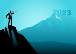 A businessman stands on a mountaintop, looking through a telescope at another mountaintop that reads “2023.”