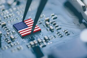 The American flag over top of a chip processer being grabbed with a pair of tweezers.