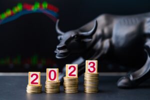 Four stacks of coins trending upward that read “2023” with a statue of a bull in the background.