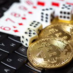 Three Bitcoin fanned out over dice and playing cards on top of a keyboard.