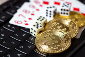 Three Bitcoin fanned out over dice and playing cards on top of a keyboard.