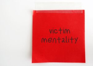 A tapped red Post-It note that reads “victim mentality” in black marker.