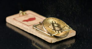 A gold Bitcoin trapped in a mousetrap.