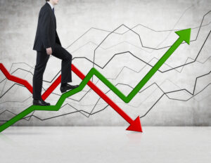 A businessman climbing a green arrow going in an upward trajectory with a red line trending downward in the background.