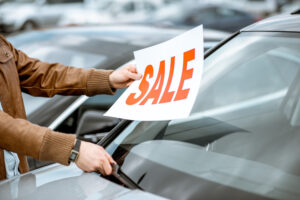 A man putting a “SALE” sign on the windshield of a car.