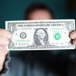 A man holding up a single dollar bill.