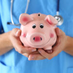 A doctor in uniform holding up a smiling pink piggy bank.
