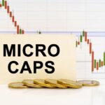 A business card that reads “MICROCAPS” in front of a downward trending line and a stack of gold coins.
