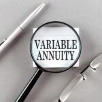 The words “VARIABLE ANNUITIES” on a note card behind a magnifying glass and other materials in the background.
