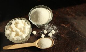A bowl of granulated sugar next to a bowl of sugar cubes with a wooden spoon in front.