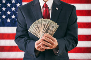 A man holding a stack of fanned-out $20 bills in front of an American flag.