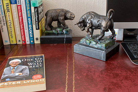 Multiple copies of books stacked on a desk with a bull and a bear figurine.