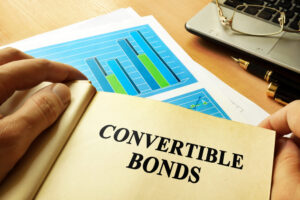 A notecard that reads “convertible bond” on top of cash and coins.