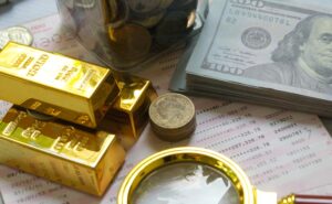 Piles of money and gold on a desk next to a magnifying glass.