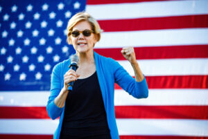 Elizabeth Warren standing in front of an American flag.