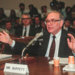 A photo of Warren Buffett with a name plate that reads “Mr. Buffett” in front of him.