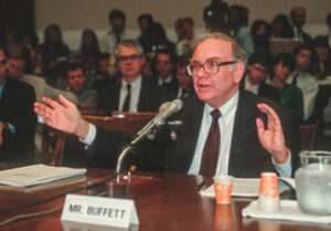 A photo of Warren Buffett with a name plate that reads “Mr. Buffett” in front of him.
