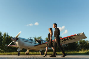 A wealthy couple dressed in all black walking in front of a plane.
