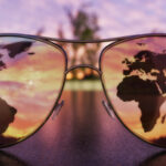 Sunglasses on a dark surface during sunrise/sunset with a reflection of a world map in the lenses.