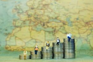 Figurines sitting on stacks of coins in front of a globe.