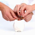 Multiple hands putting coins into a piggy bank.