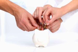 Multiple hands putting coins into a piggy bank.