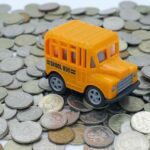 A toy school bus on top of a pile coins.