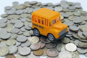 A toy school bus on top of a pile coins.