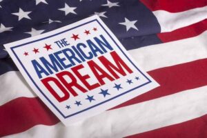 A sign that says “The American Dream” overtop of an American flag.