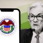 A phone screen showing the Fed symbol with Jerome Powell in the background.