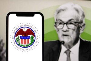 A phone screen showing the Fed symbol with Jerome Powell in the background.