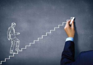 A close up of a human hand drawing a man climbing a ladder with chalk.