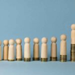 Wooden figurines on top of stacks of coins.